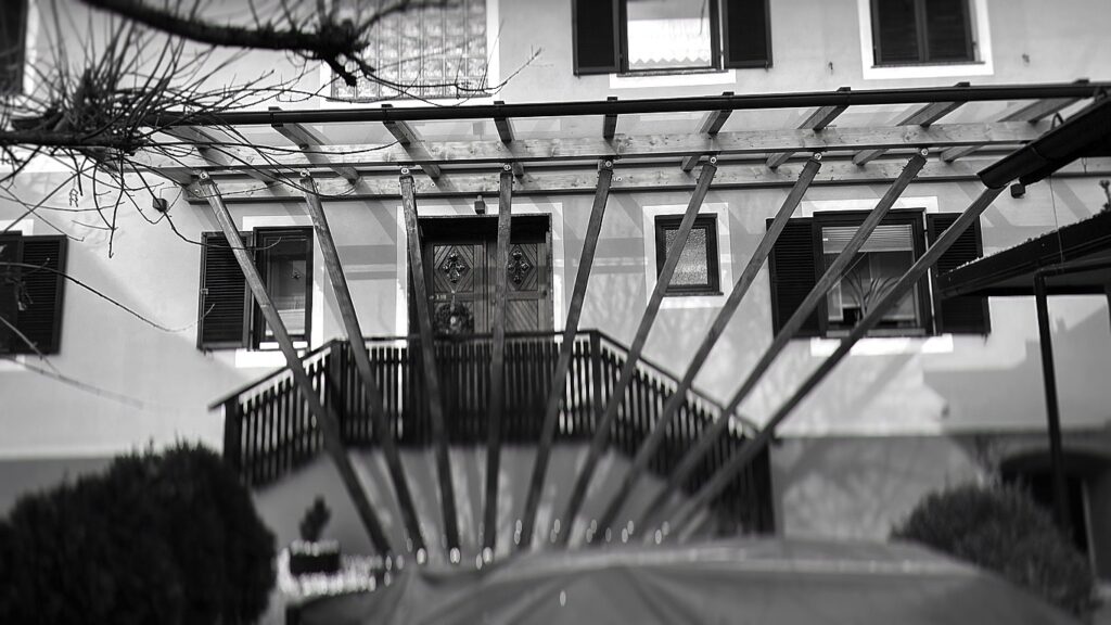 Vordach als radial konstruiertes System mit zentralem Bezugspunkt vor dem Eingang, rückverankert über schräge Stützen am Wirtschaftsgebäude – Haus T in Prebuch – aha. architektur Andreas Haselgruber